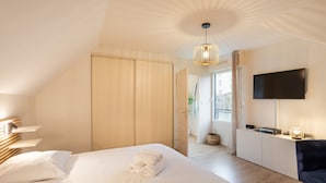 A modern bedroom with a large bed, a flat-screen TV, and a ceiling light fixture. - La Petite Maison Dans la Prairie - Havre de paix (Rennes)