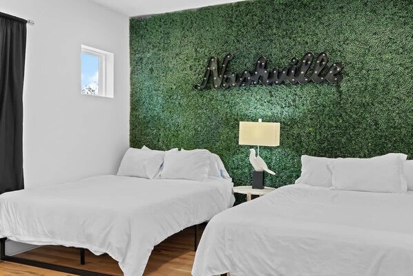 Habitación de hotel con dos camas, una pared verde con una placa, un ventanal pequeño y una mesita de noche con lámpara.