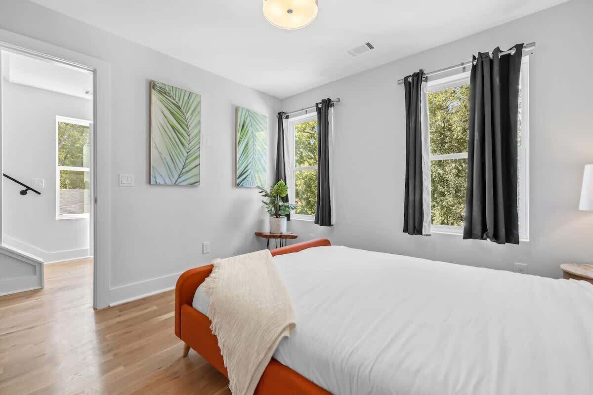 A bedroom with a bed, a nightstand, a potted plant, and a window with curtains.