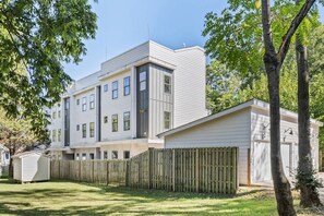 Un edificio residencial moderno de varios pisos con un patio cercado y un cobertizo pequeño.