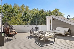 En takterrass med en vit soffa, två metallstolar och en hängstol.