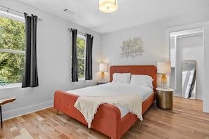 Un dormitorio con cama, dos mesitas de noche, un espejo y una ventana con cortinas.