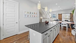 A modern kitchen with a central island, pendant lighting, and a staircase leading to a loft area. - Rooftop Views! Luxury East Nash 3 BR Townehome (Nashville)