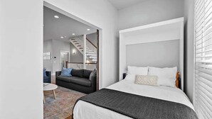 A modern bedroom with a large bed, a small seating area, and a staircase leading to an upper level. - Rooftop Views! Luxury East Nash 3 BR Townehome (Nashville)