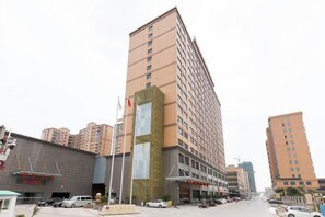 Un hotel de varios pisos con fachada moderna, asta de bandera y zona de estacionamiento.