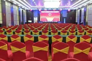 A conference room with rows of tables and chairs, a stage with a large screen, and a red carpeted floor. - Jukai International Hotel (Nan'an)