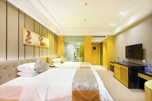 Habitación de hotel con cama, televisión, escritorio y baño visible a través de una puerta de cristal.