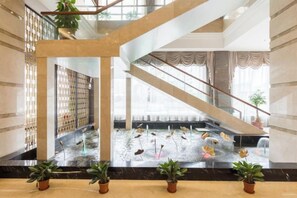 A hotel lobby with a staircase, potted plants, and a decorative water feature.