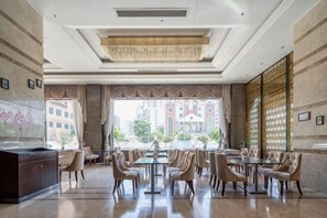 Un hall d’hôtel spacieux avec un grand espace dédié à la restauration, un comptoir d’accueil et une vue sur le paysage urbain.