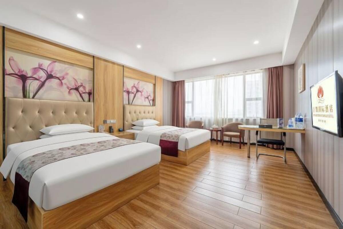 A hotel room with three beds, a desk, and a TV.