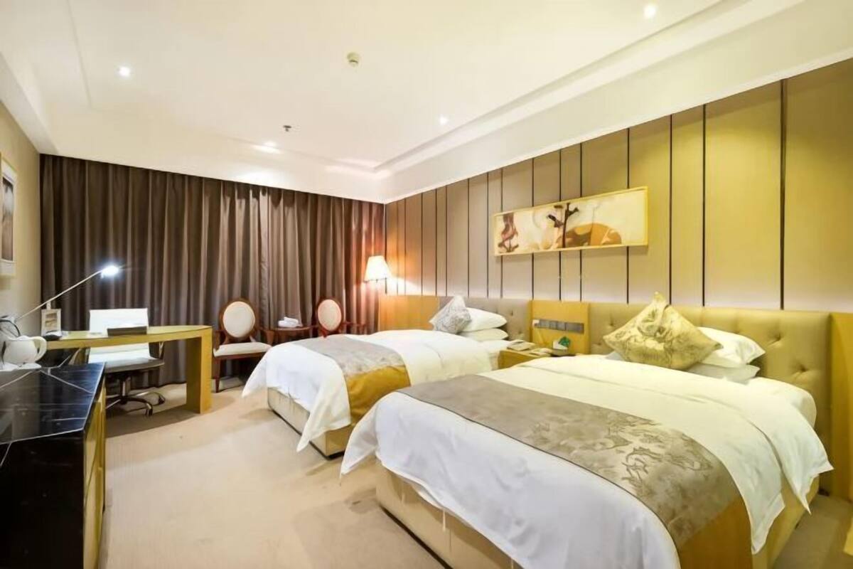 A hotel room with two beds, a desk, a chair, and a lamp.