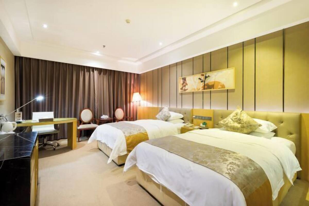 A hotel room with two beds, a desk, a chair, a lamp, and a painting on the wall.