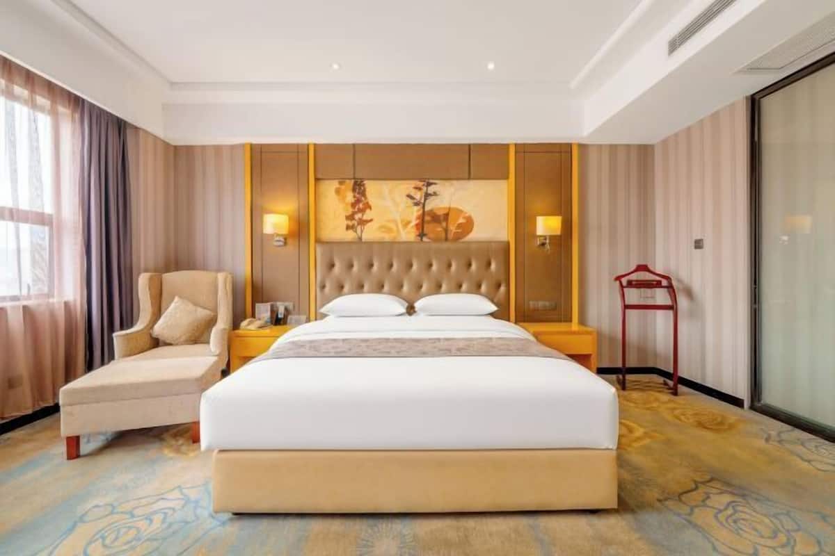 A hotel room with a large bed, a chair, a nightstand, and a wall-mounted lamp.
