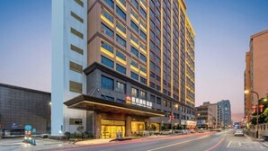 Een meerlaags hotel met een opvallende ingang, een open weg ervoor en aangrenzende gebouwen.