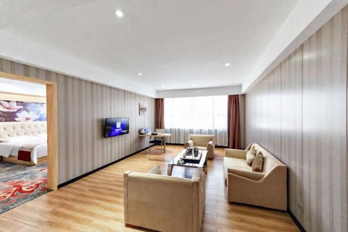 A modern hotel room with a flat-screen TV, a sofa, a coffee table, and a bed with a red accent pillow.