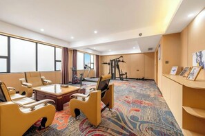 A hotel room with a large bed, a desk, two chairs, a treadmill, and a wall-mounted TV.