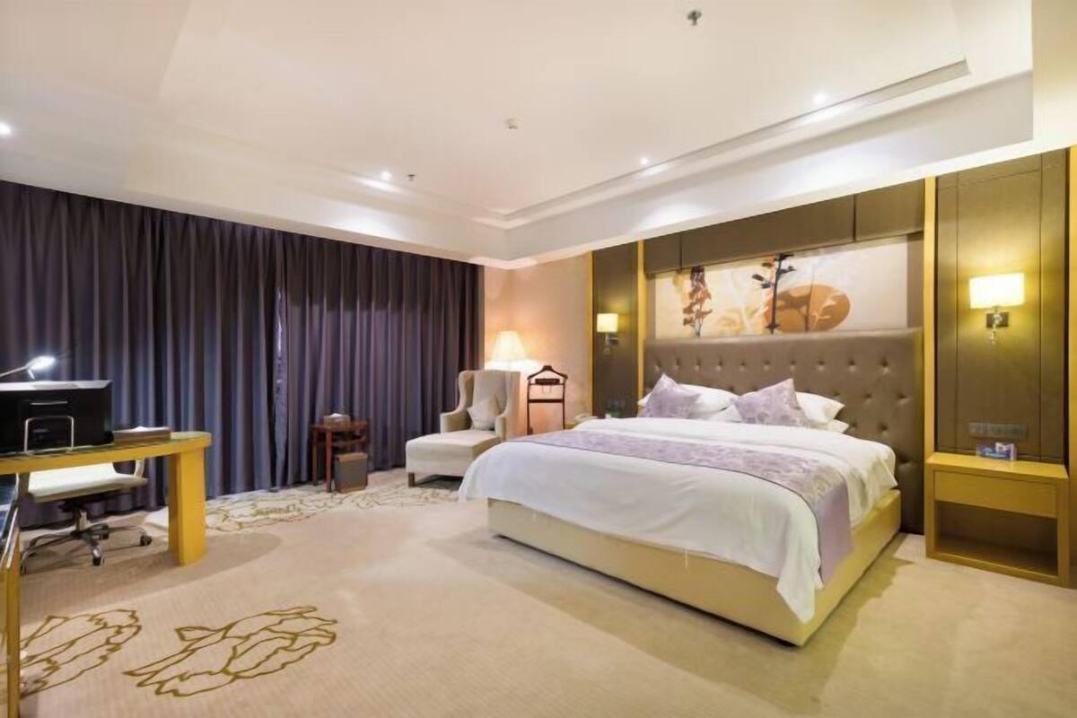 A hotel room with a bed, a desk, a chair, and a TV.