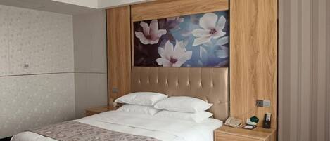 A hotel room with a bed, a nightstand, a telephone, and a small shelf.