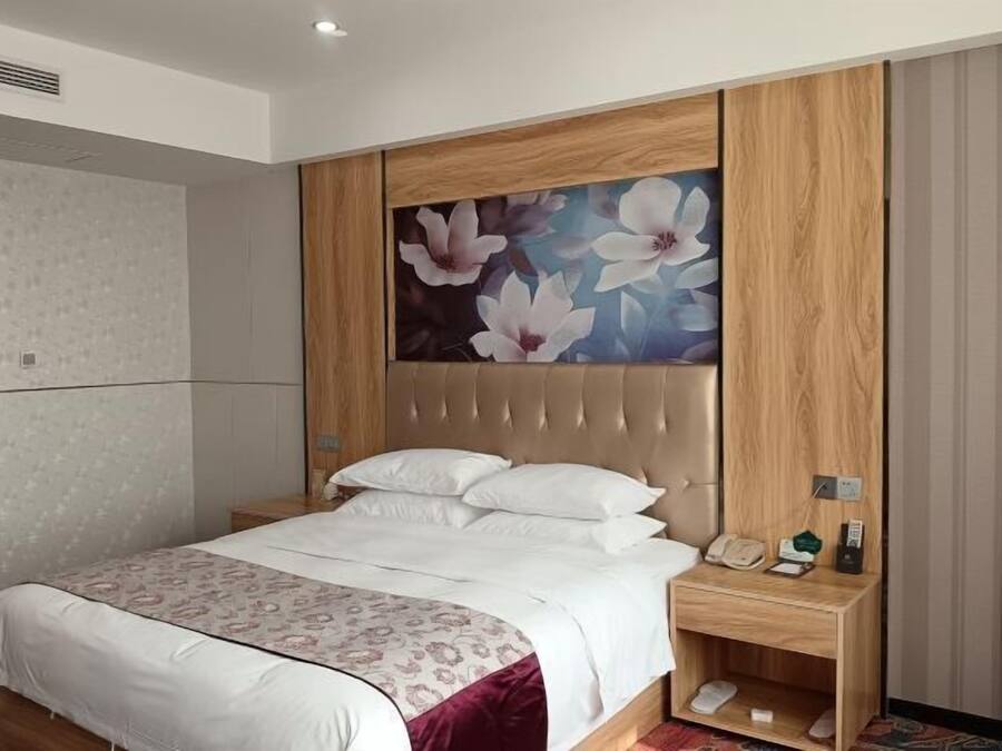 A hotel room with a bed, a nightstand, a telephone, and a small shelf.