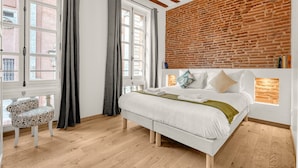 A bedroom with a large bed, a brick wall, and a window with curtains.