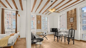 A modern room with exposed wooden beams, a sofa, a dining table with chairs, and a TV.