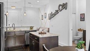 Une cuisine moderne dotée d’un îlot central, d’appareils électroménagers en acier inoxydable, de luminaires suspendus et d’un panneau décoratif fixé au mur.