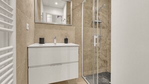 A modern bathroom with a glass shower enclosure, a white vanity with a mirror, and beige tiled walls. - Frère Jacques - Appt situé plein centre (Toulouse)