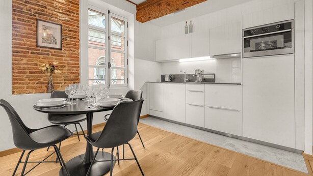 A modern kitchen with white cabinets, a built-in oven, and a dining area with a table and chairs. - Frère Jacques - Appt situé plein centre (Toulouse)