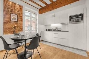A modern kitchen with white cabinets, a built-in oven, and a dining area with a table and chairs. - Frère Jacques - Appt situé plein centre (Toulouse)