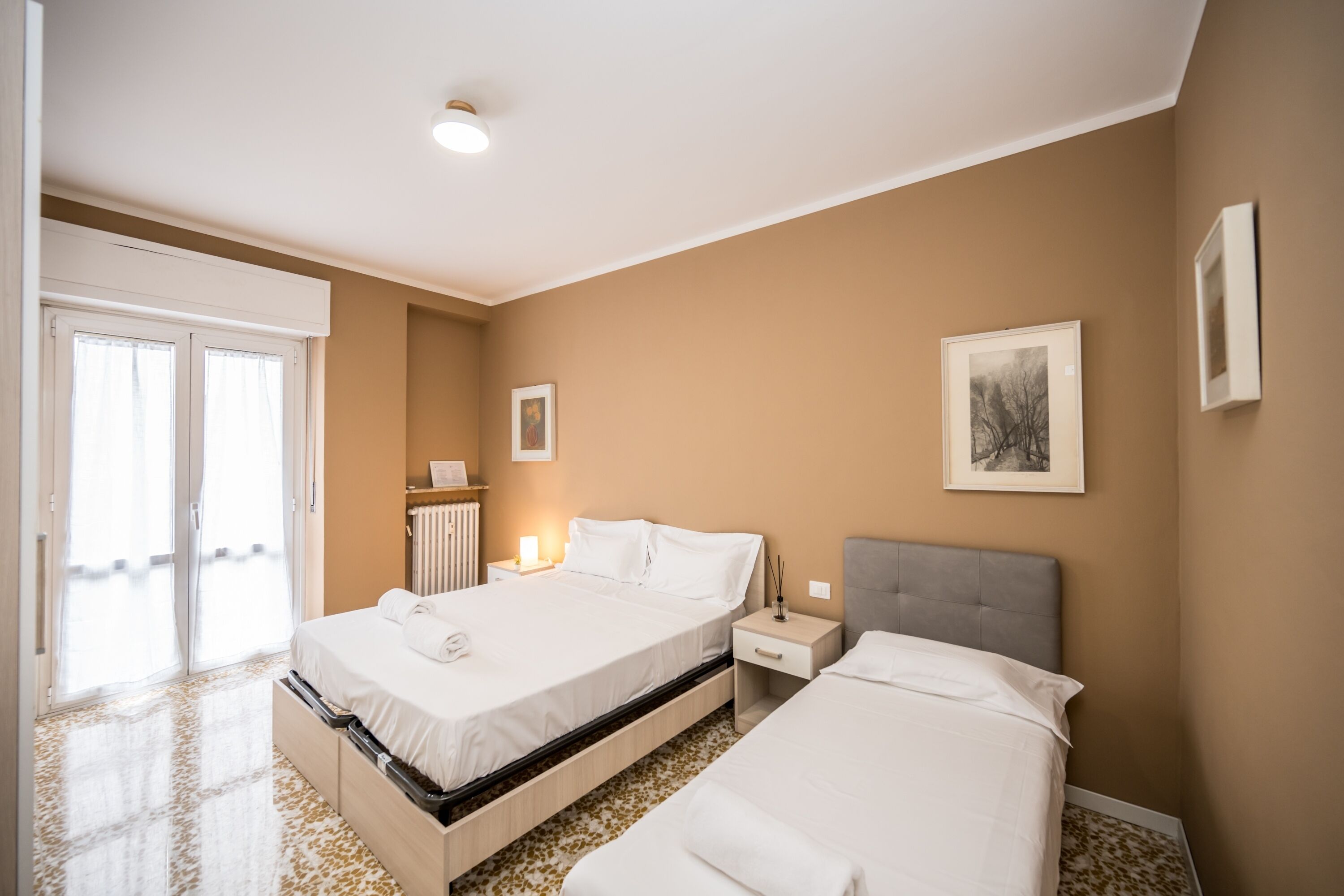 Ein Hotelzimmer mit zwei Betten, einem Heizkörper, einem Nachttisch und einem gerahmten Bild an der Wand.