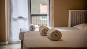 Een hotelkamer met een bed, een raam met uitzicht op gebouwen en een deur die leidt naar een buitenruimte.