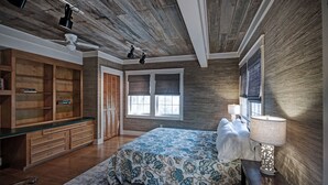 Un dormitorio con techo de madera, una cama con colcha estampada, una mesita de noche con lámpara y un armario grande.