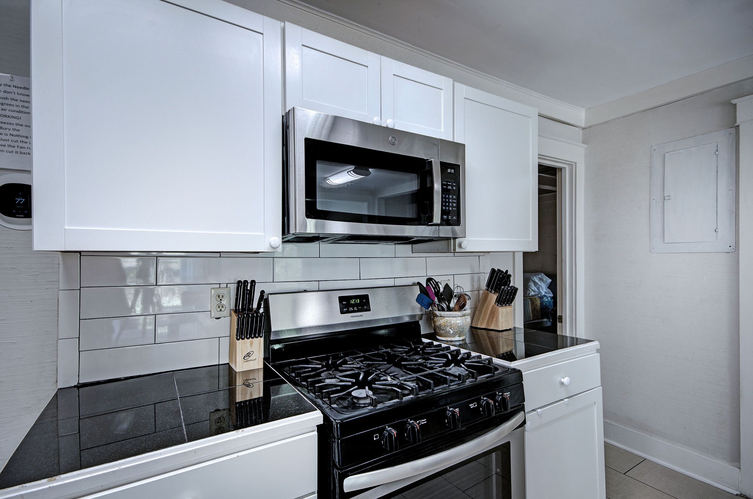 A kitchen with white cabinets, a stainless steel microwave, a black gas stove, and a white oven.