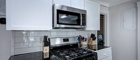 A kitchen with white cabinets, a stainless steel microwave, a black gas stove, and a white oven.
