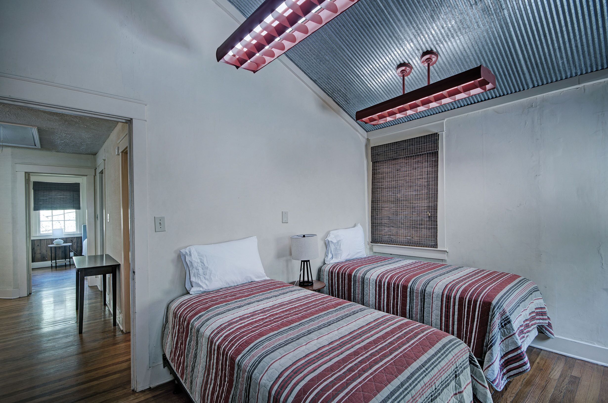 Ein Zimmer mit zwei Betten, einem Tisch, einer Lampe und einem Fenster mit Jalousien.