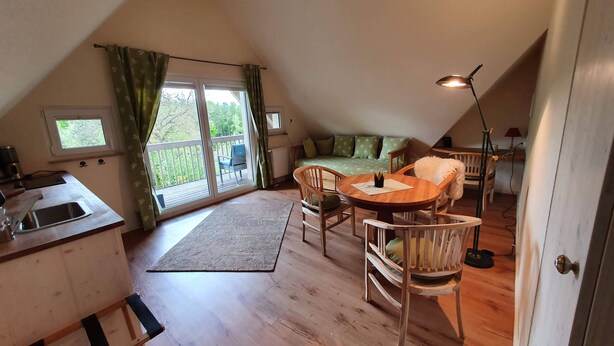 A cozy attic bedroom with a wooden floor, a dining table, and a sofa.