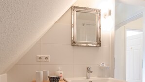 A bathroom with a white sink, a mirror, a wooden shelf with toiletries, and two white buckets.
