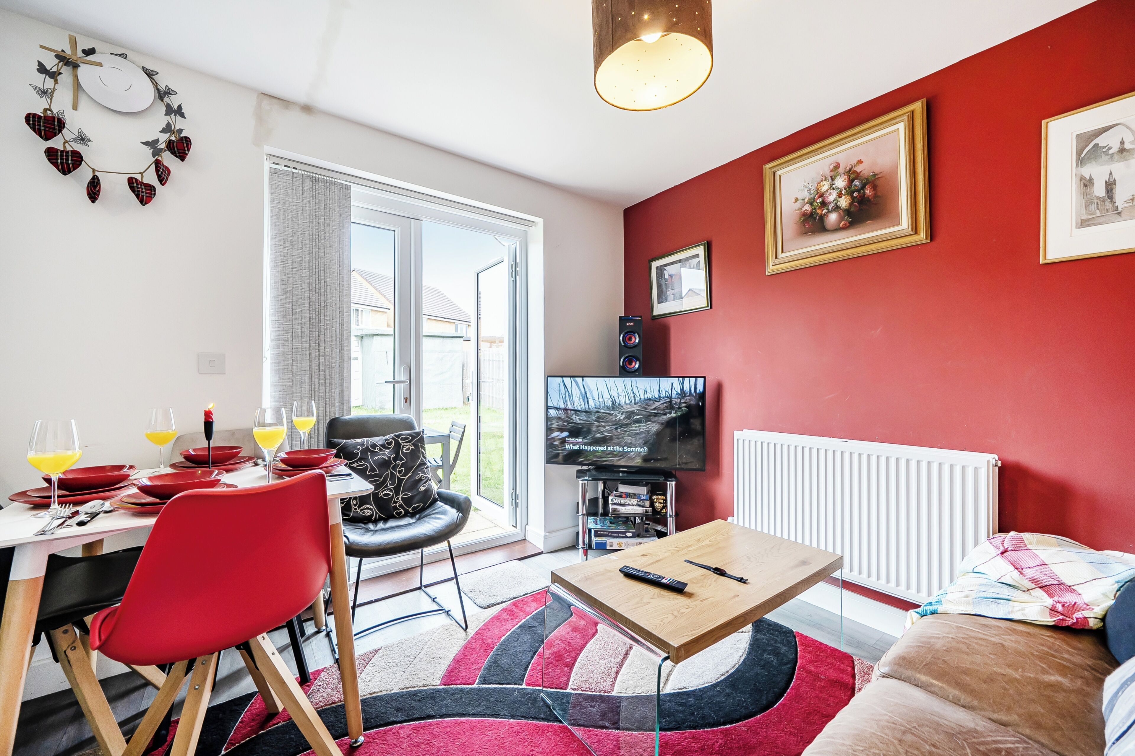 A living room with a dining area, red walls, a television, and a view through a glass door.