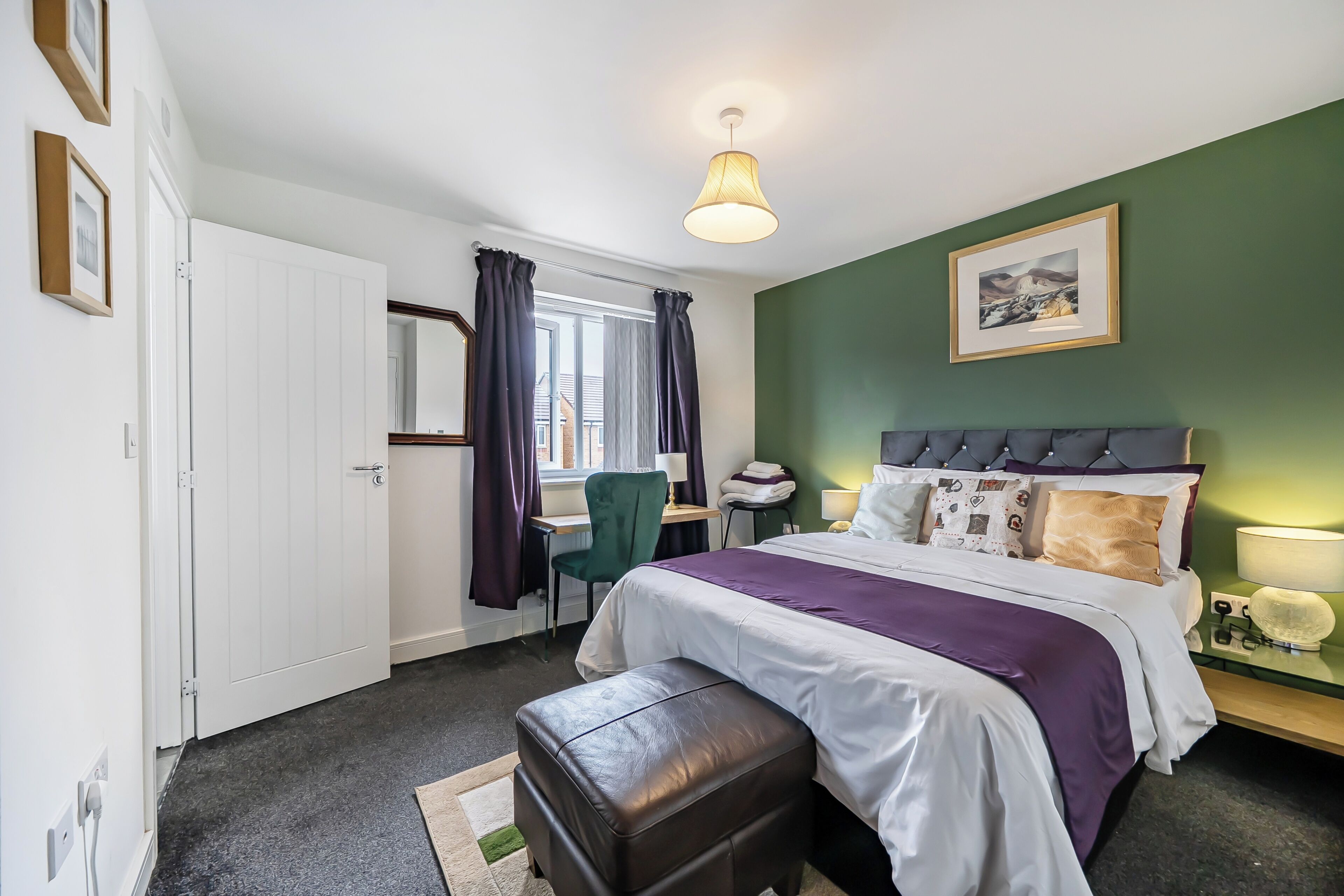 A bedroom with a bed, a desk, a chair, a window with curtains, and a green wall.