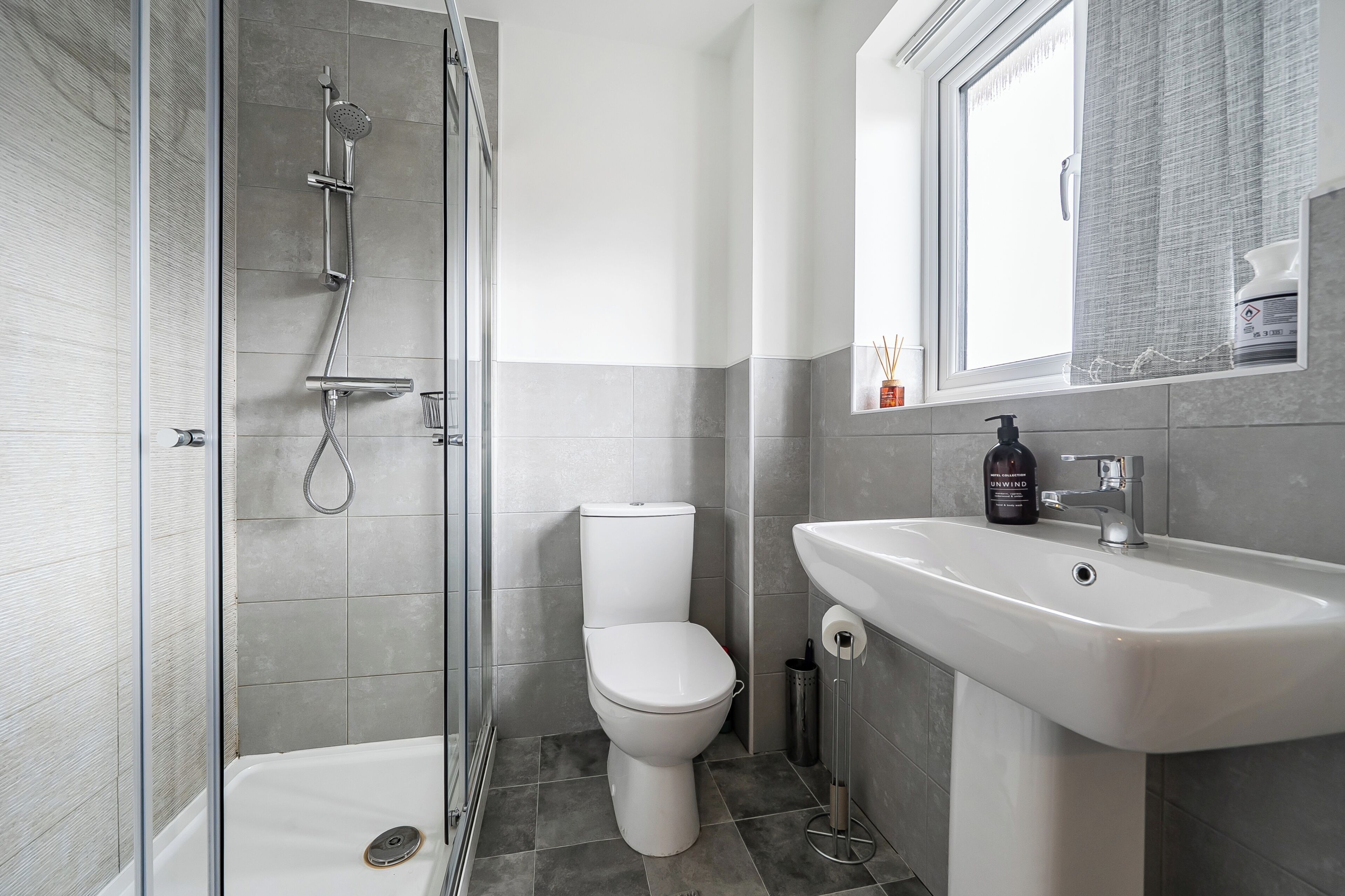 A modern bathroom with a glass-enclosed shower, a white toilet, and a pedestal sink.