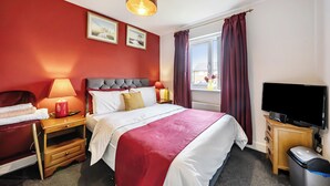 Une chambre d’hôtel avec un lit, des tables de chevet, une télévision, une fenêtre avec des rideaux et des œuvres d’art au mur.