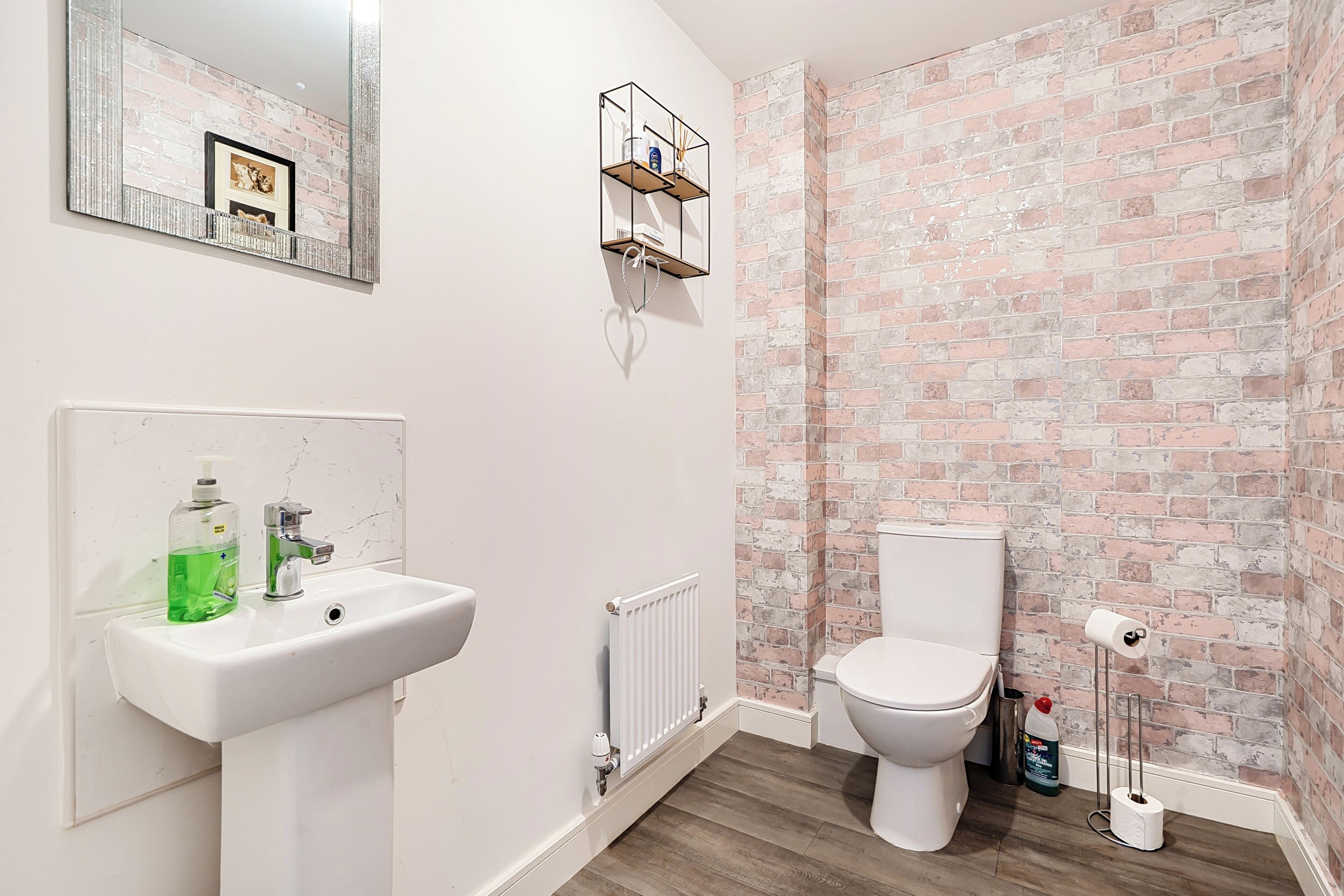 A bathroom with a white sink, a toilet, a radiator, and a brick-patterned wall.