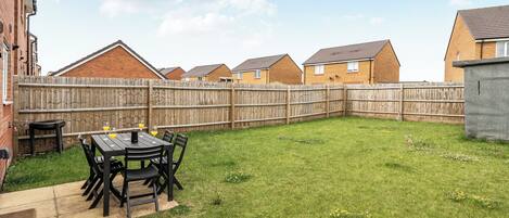 A backyard with a patio table and chairs, a wooden fence, and houses in the background.