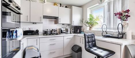 Een moderne keuken met witte kastjes, een zwarte barstoel, een raam met uitzicht en een potplant.