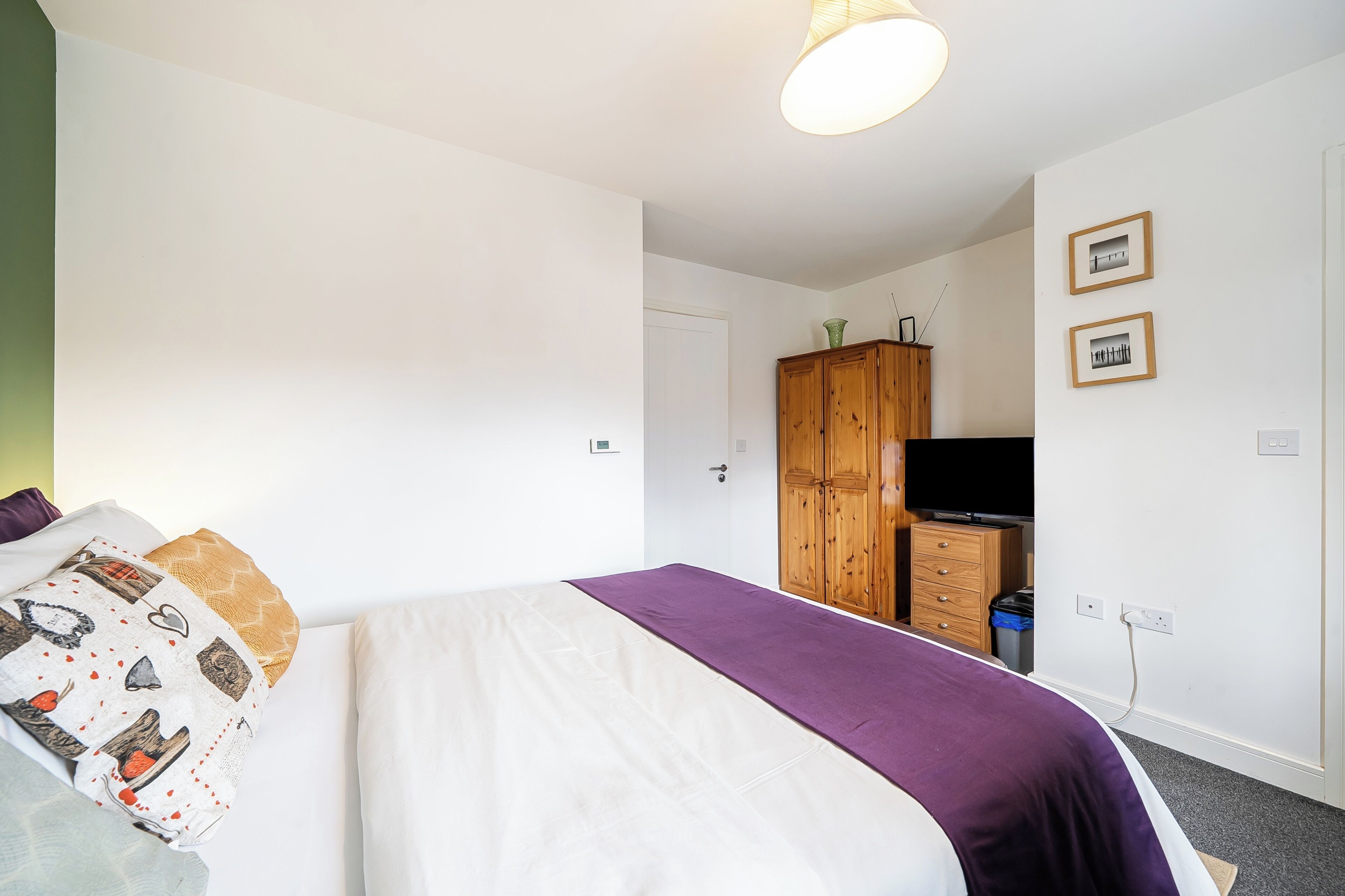 A bedroom with a bed, a wardrobe, a television, and a door.