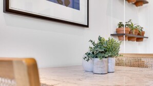 Una mesa de comedor con tapa de mármol, rodeada de sillas de mimbre. Hay tres plantas en macetas sobre la mesa.