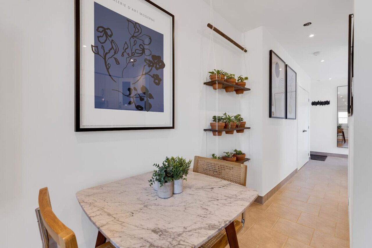 Ein modernes Interieur mit einem Marmortisch, Zimmerpflanzen und gerahmten Kunstwerken an den Wänden.