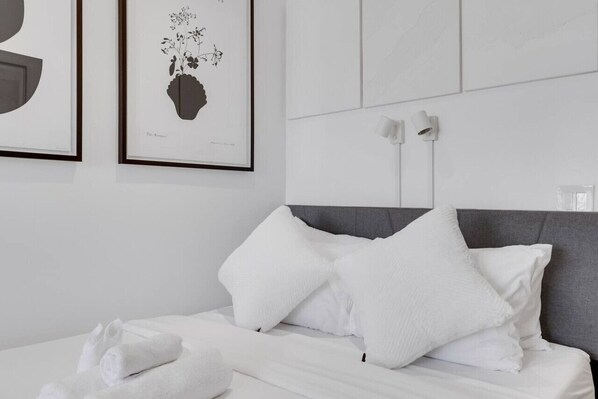 Una habitación de hotel moderna con una cama bien hecha, toallas blancas y dos cuadros enmarcados en la pared.