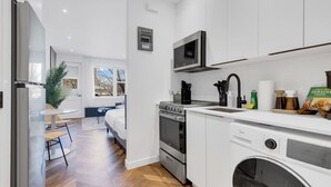 A modern kitchen with white cabinets, stainless steel appliances, and a built-in washing machine. - Downtown Montreal Speakeasy 502 | Balcony, Queen Bed, Sofa Bed, Parking & 65` TV (Montreal)