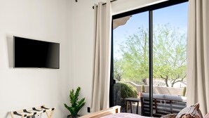 Ein Hotelzimmer mit Bett, Wand-Fernseher, Fenster mit Blick auf Bäume und eine Kaktee, sowie ein kleiner Tisch mit Pflanze.